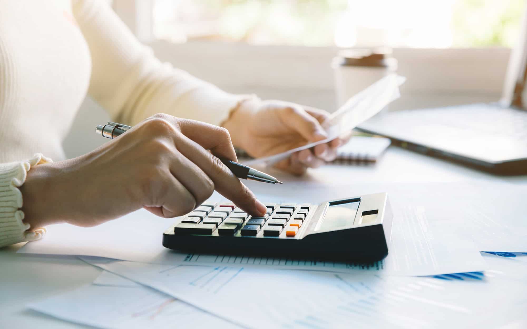 Side view of a woman in yellow shirt using a calculator while doing taxes