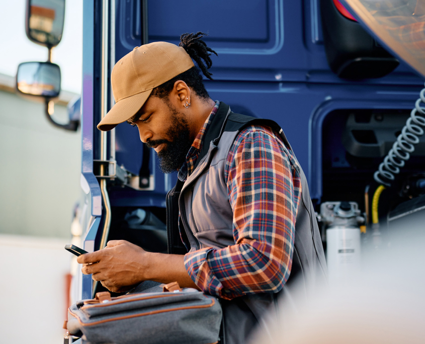 Side view of a truck driver texting while standing near his semitruck