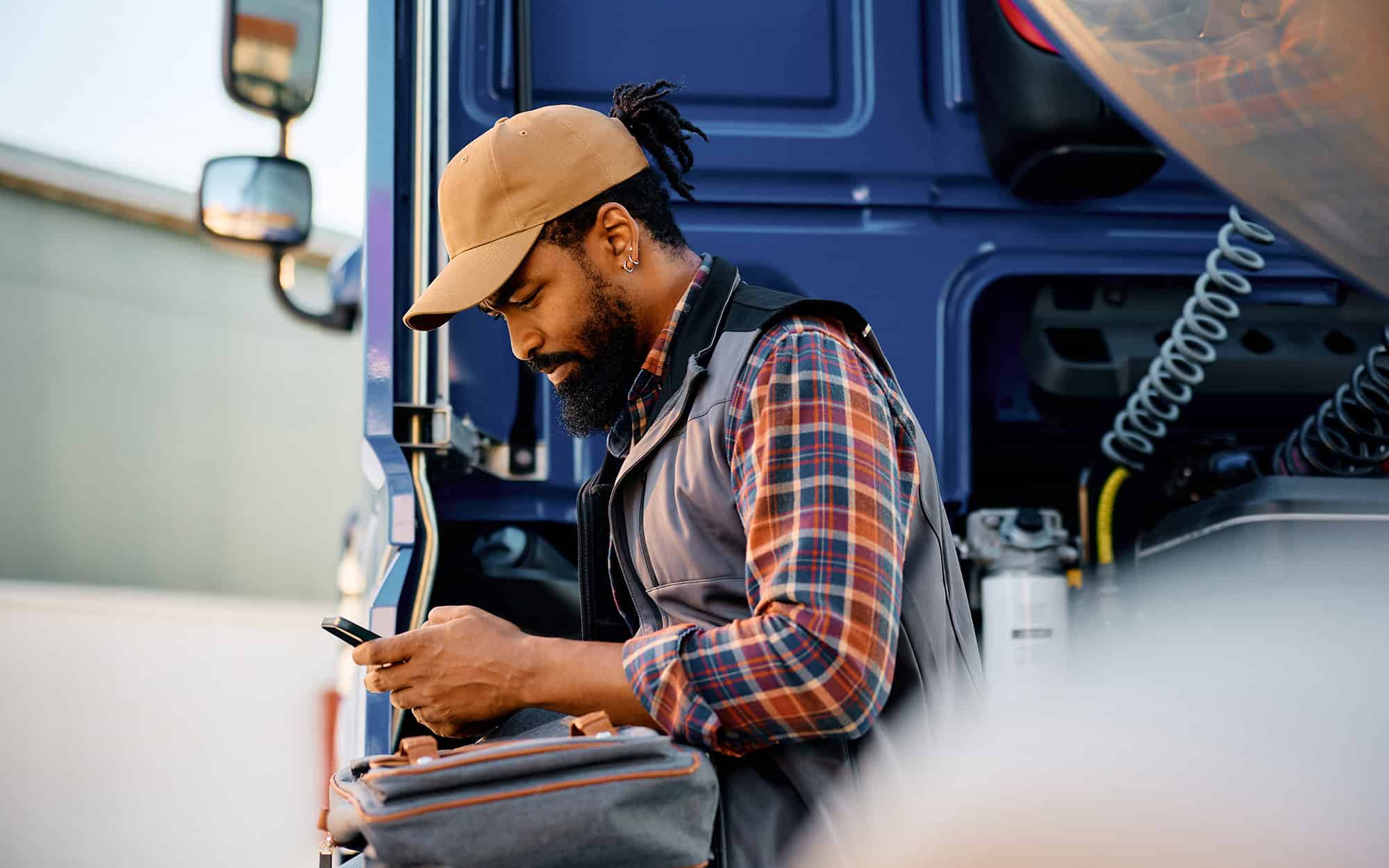 Side view of a truck driver texting while standing near his semitruck