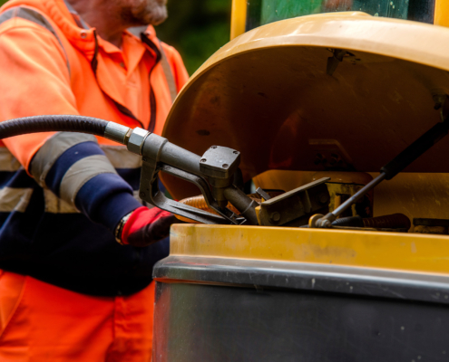 Builder in safety gloves filling excavator with diesel fuel on building site