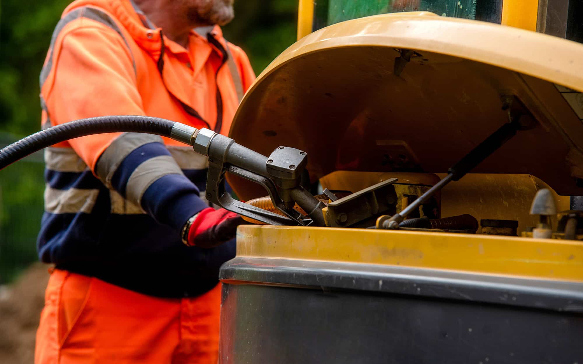 Builder in safety gloves filling excavator with diesel fuel on building site