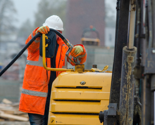 Construction worker in safety gloves filling excavator with diesel fuel on building site