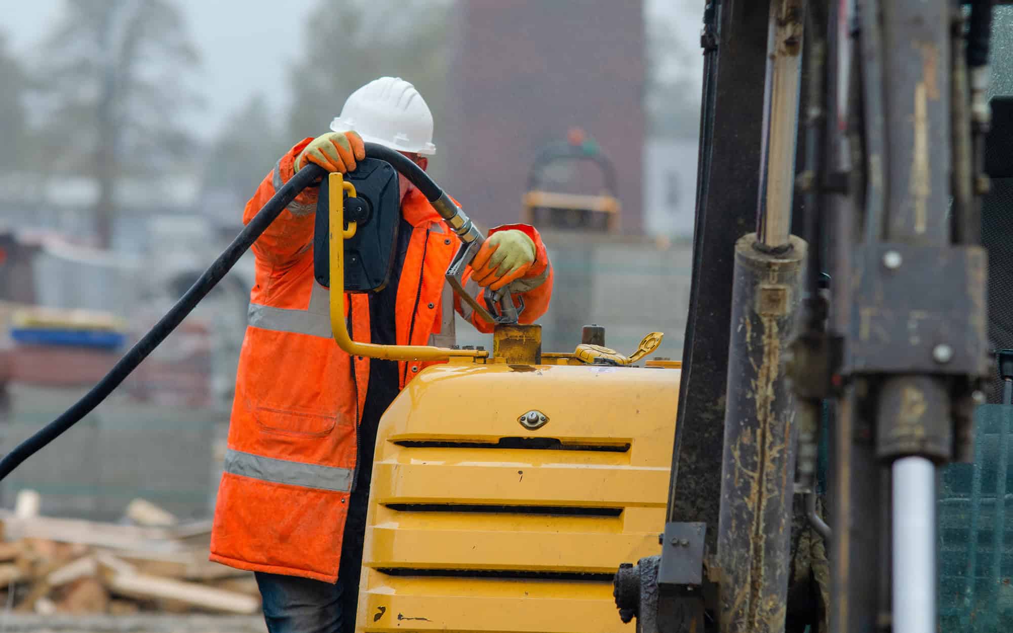 Construction worker in safety gloves filling excavator with diesel fuel on building site