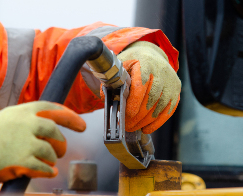 Construction worker in safety gloves filling excavator with diesel fuel on construction site